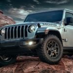 A silver 2018 Used Jeep Wrangler Moab is parked on dark rocks in front of stormy clouds.