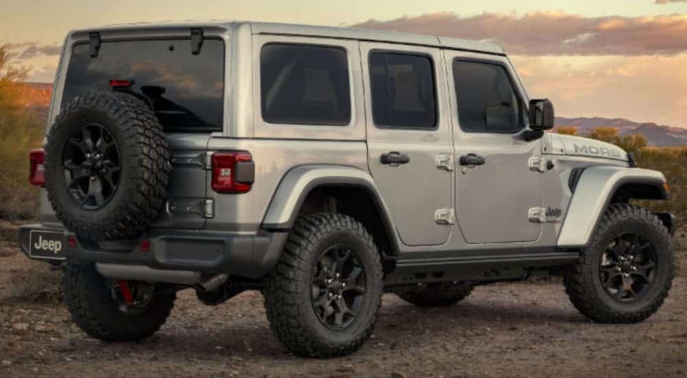 A silver 2018 Used Jeep Wrangler Moab is shown from the rear off-road in front of a sunset.