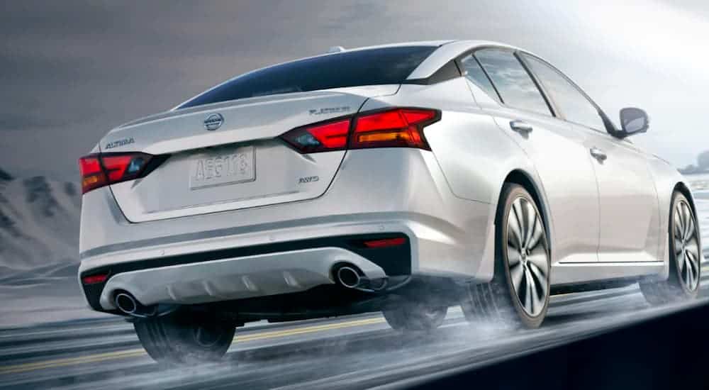 A white 2019 used Nissan Altima is shown from the rear driving on a wet road.