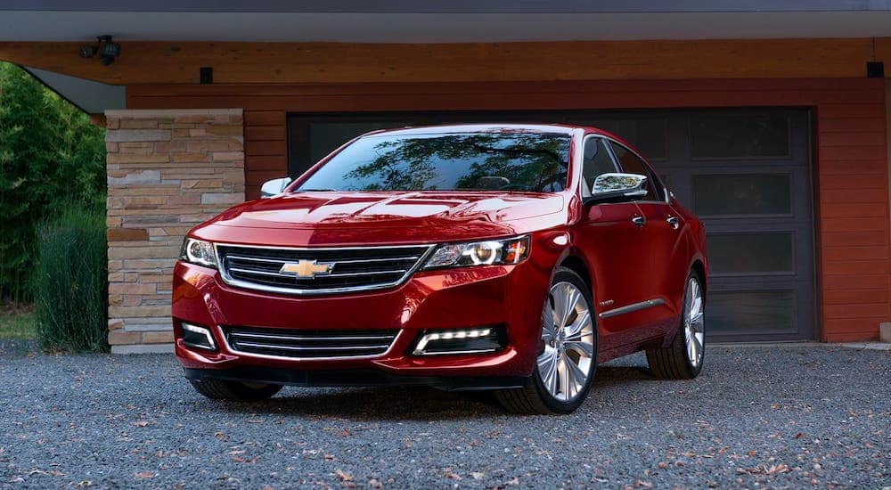 A red 2020 Chevy Impala is parked in front of a garage.