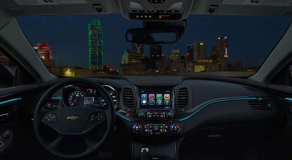 The dashboard and black interior with blue accents are shown in a 2020 Chevy Impala at night.