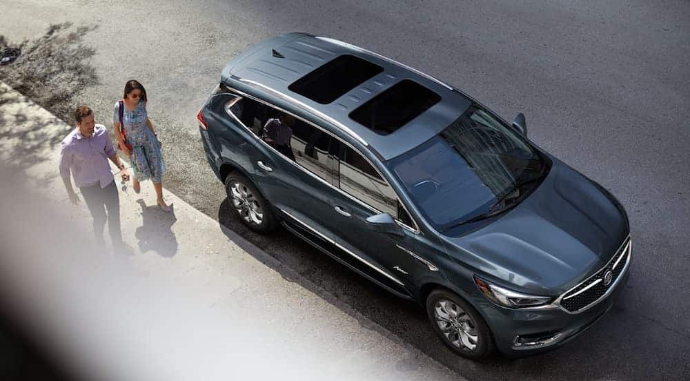 A couple is walking past a grey 2021 Buick Enclave Avenir shown from above on a city street.