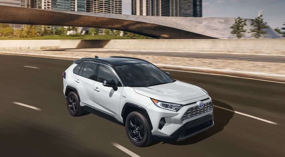 A white 2021 Toyota RAV4 XSE is driving on the highway past a bridge.