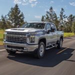 A silver 2021 Chevy Silverado 2500HD is driving on a highway past grass and trees.