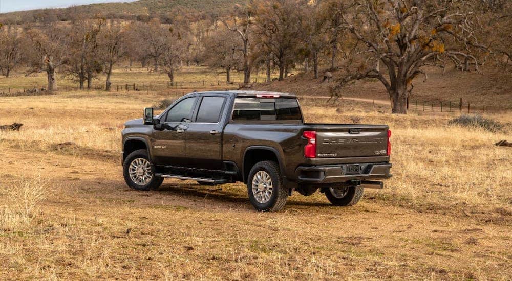 A black 2021 Chevy Silverado 2500HD High Country is facing away while parked on yellow grass.