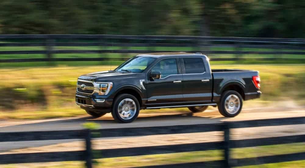 A black 2021 Ford F-150 is driving in front of a fence.