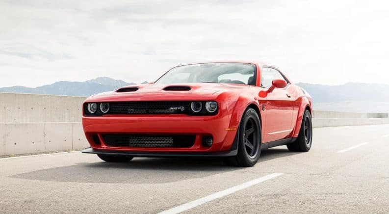An orange 2021 Dodge Challenger is driving down an empty highway past a concrete wall.