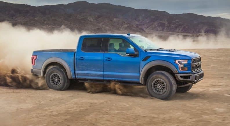 A blue 2020 Ford Raptor is driving on dirt and shown from the side.