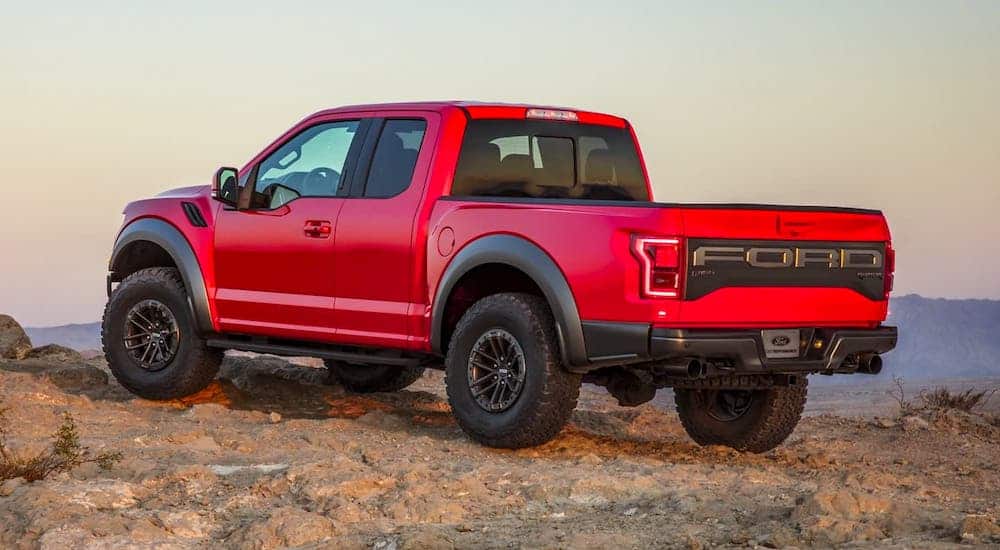 A red 2020 Ford Raptor, similar to a 2021 Ford Raptor, is facing away while parked on rocks.