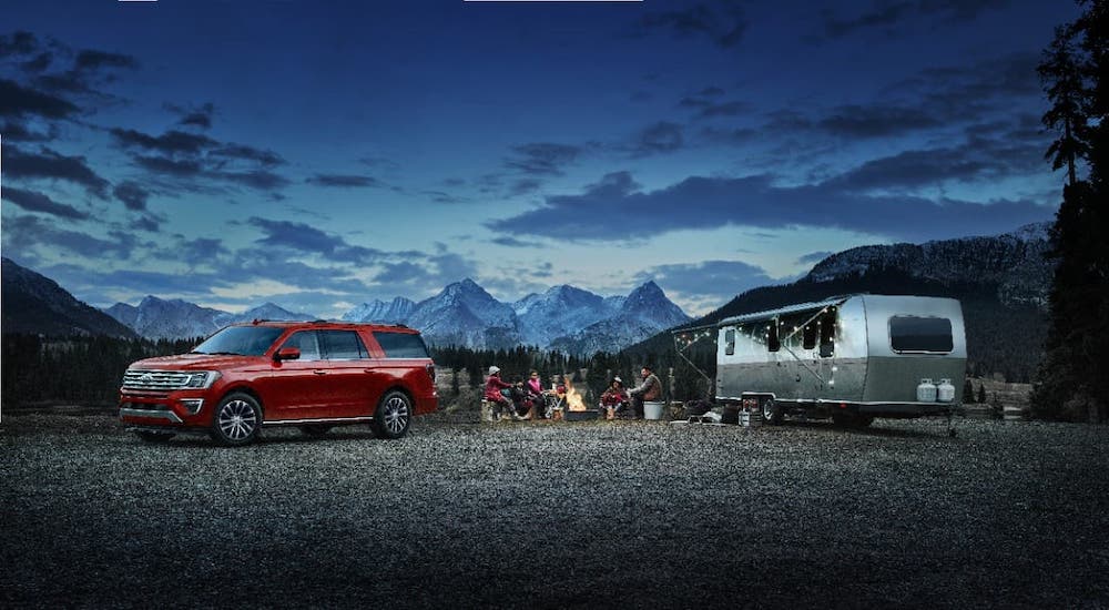 A red 2021 Ford Expedition is parked at a campsite at night next to an Airstream camper.