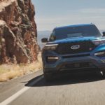 A blue 2021 Ford Explorer Hybrid is shown from the front while driving next to a rock face.