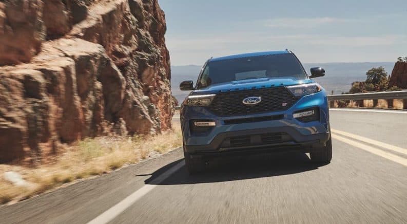 A blue 2021 Ford Explorer Hybrid is shown from the front while driving next to a rock face.