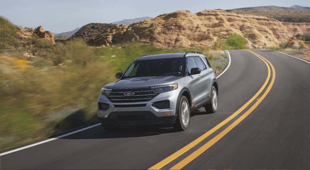 A silver 2021 Ford Explorer Hybrid is driving on a desert highway.