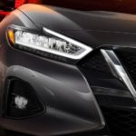 A close up is shown of the headlight and grille on a dark grey 2021 Nissan Maxima