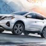 A white 2021 Nissan Murano is driving around a corner up a snowy road.