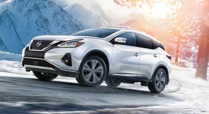 A white 2021 Nissan Murano is driving around a corner up a snowy road.