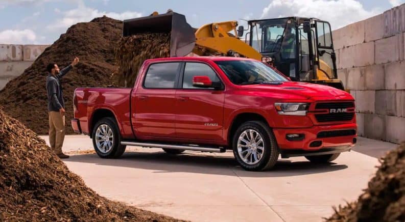 A man is guiding a loader driver who is loading mulch into the bed of a red 2021 Ram 1500.