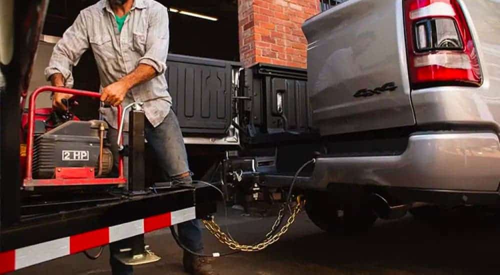 A man is loading equipment from a trailer into the bed of a silver 2021 Ram 1500 using the Multifunction tailgate.