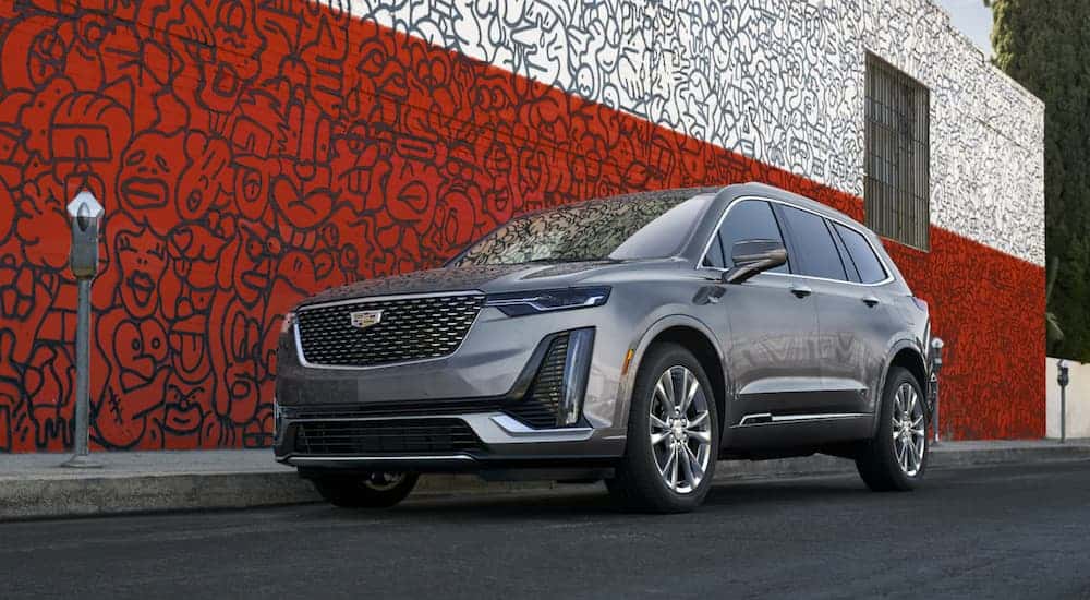 A grey 2021 Cadillac XT6 is parked in front of a red and white wall with art on it after leaving a Cadillac dealer near me.