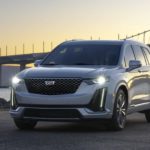 A silver 2021 Cadillac XT6 is parked in front of a bridge at sunset.