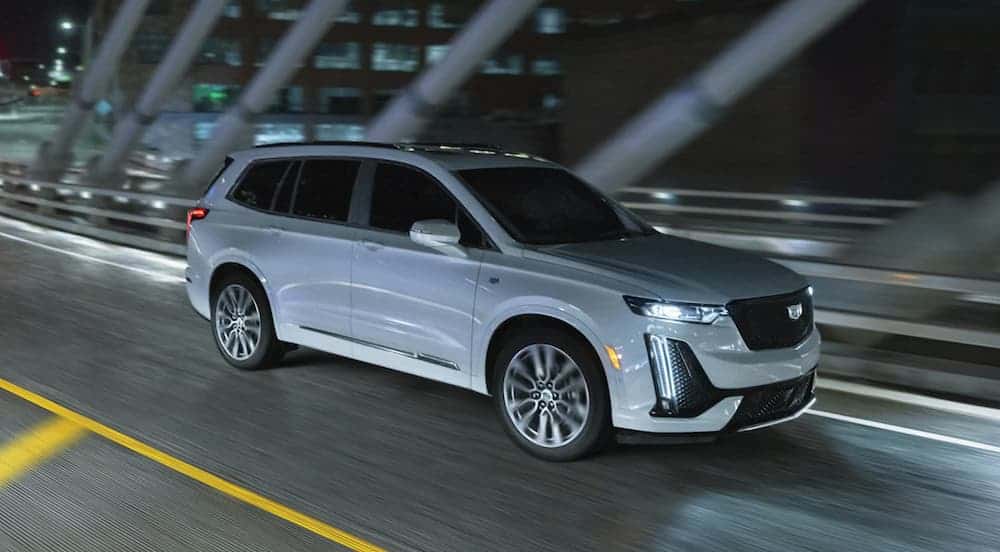 A white 2021 Cadillac XT6 is driving on a city bridge at night.
