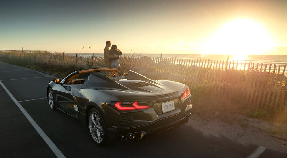 A couple is shown on the coast at sunset next to a grey 2021 Chevy Corvette.