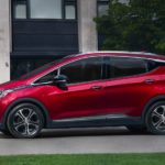 A red 2021 Chevy Bolt EV is shown from the side, parked in front of flower planters.