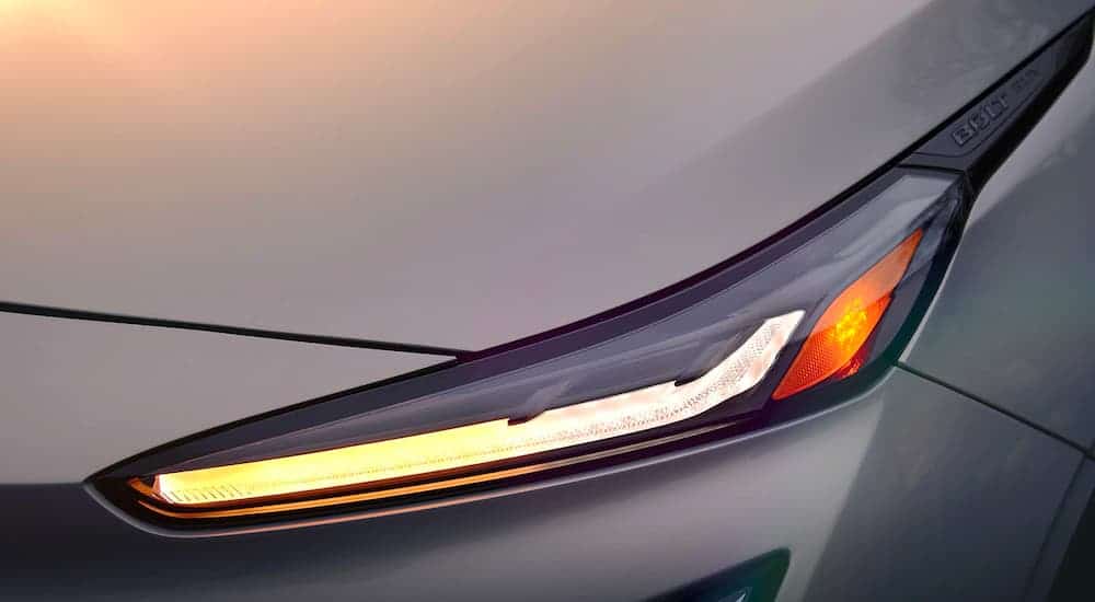 A exciting new Chevy EV, a white 2022 Chevy Bolt EUV, is shown with a close up of the front driver headlight and badging.