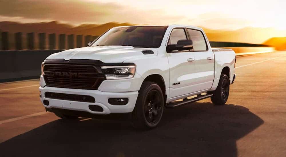 A white 2021 Ram 1500 Night Edition is driving down the road at sunset after leaving a Cincinnati Ram diesel truck dealer.