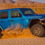 A blue 2021 Jeep Wrangler Rubicon 392 is driving though the desert kicking up sand.