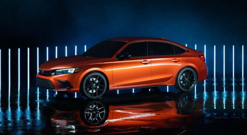 An orange 2022 Honda Civic prototype is parked in a dark warehouse in front of neon lights.