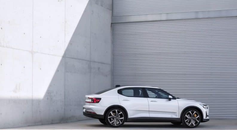 A white 2021 Polestar 2 is shown from the side parked next to a metal and concrete wall.