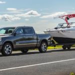 A gray 2021 Ram 1500 is towing a boat in front of a lake.