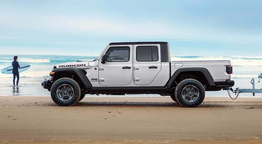 A silver 2021 Jeep Gladiator from a Southern California Jeep dealer is parked in front of a surfer and the ocean.