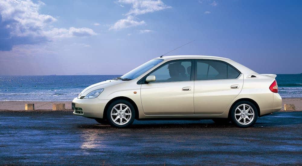 A pearl-colored 1st gen Toyota Prius is parked in front of an ocean.