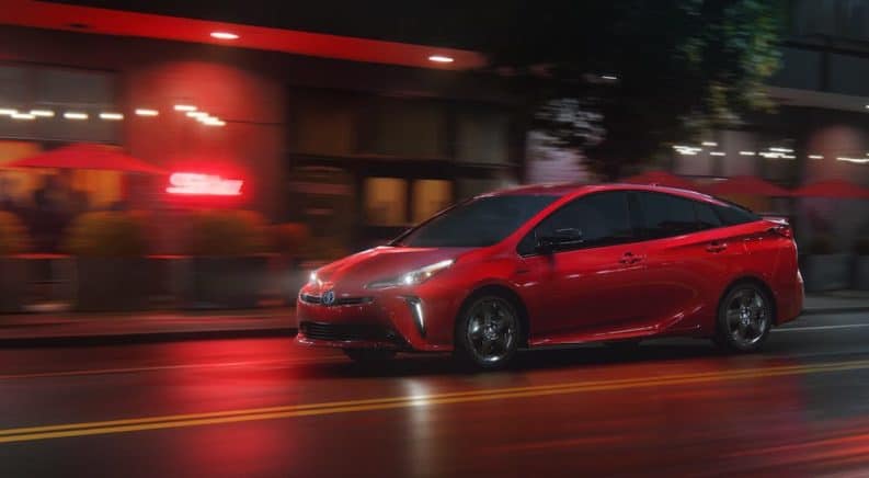 A red 2021 Toyota Prius is driving on a city street at night after leaving a Toyota Prius dealership.