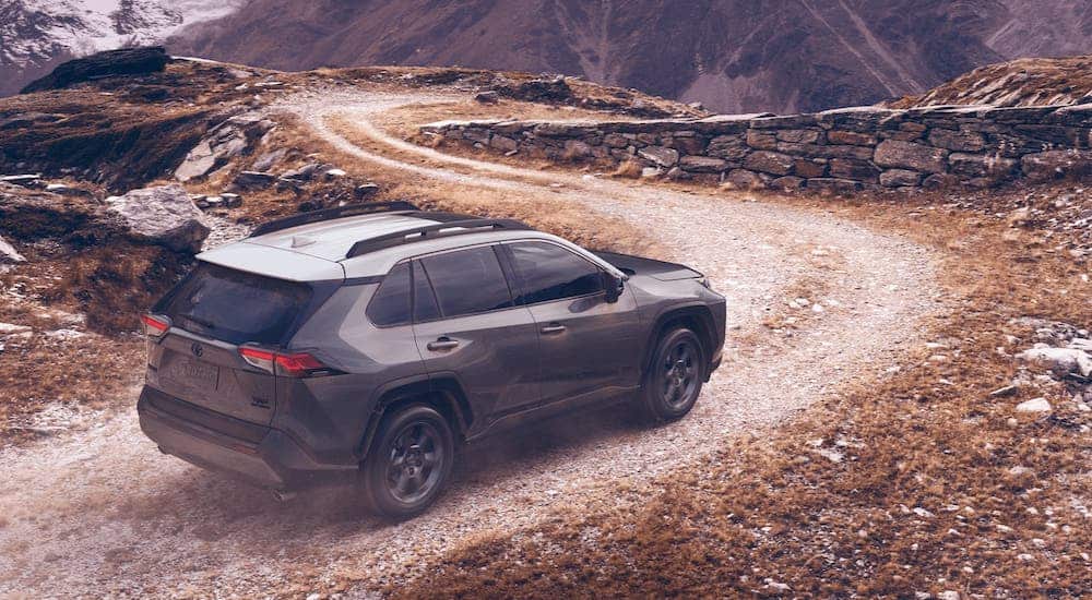 A gray 2021 Toyota RAV4 Hybrid is driving on a dirt road towards a stone wall.