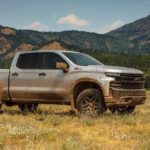 A silver 2021 Chevy Silverado TrailBoss is covered in mud and parked in a field with yellow grass.