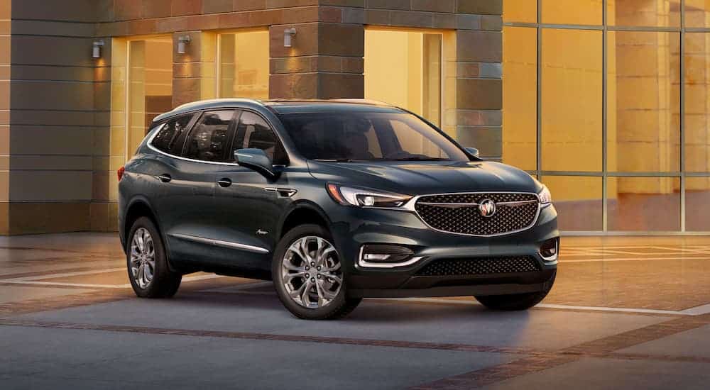 A dark gray 2019 used Buick Enclave Avenir is parked in front of a brick and glass building.