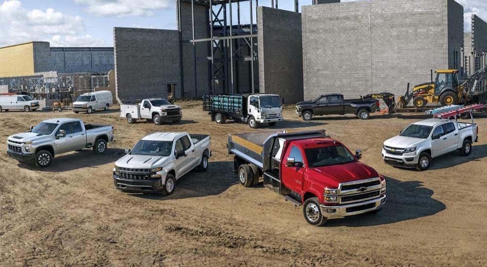 The lineup of silver, white and red Chevy commercial vehicles are shown at a job site.