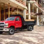 A red 2021 Chevy Silverado 5500 dump truck is parked in front at a construction site.