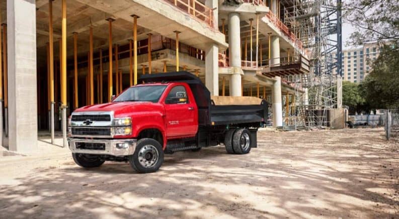 A red 2021 Chevy Silverado 5500 dump truck is parked in front at a construction site.