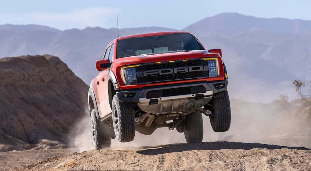 A red 2021 Ford F-150 Raptor is hitting a jump while off-roading in the desert.