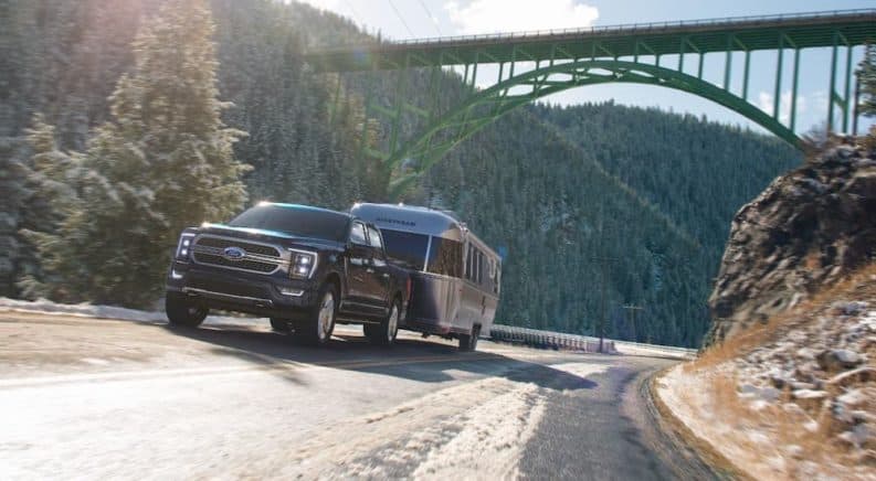 A black 2021 Ford F-150 is towing an Airstream camper under a large bridge.