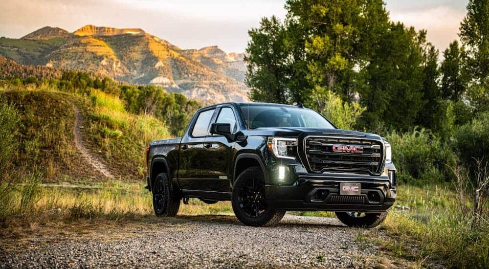 A black 2021 GMC Sierra Elevation is parked on a dirt trail in front of trees and hills after losing the 2021 Ford F-150 vs 2021 GMC Sierra 1500 comparison.