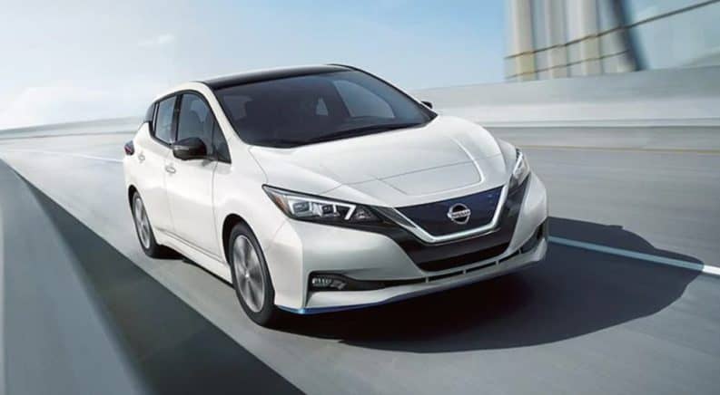 A white 2021 Nissan LEAF is driving on a highway overpass.