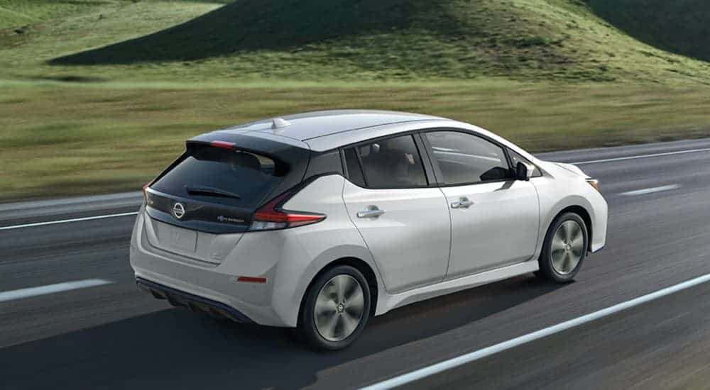 A white 2021 Nissan LEAF is driving past grassy hills.