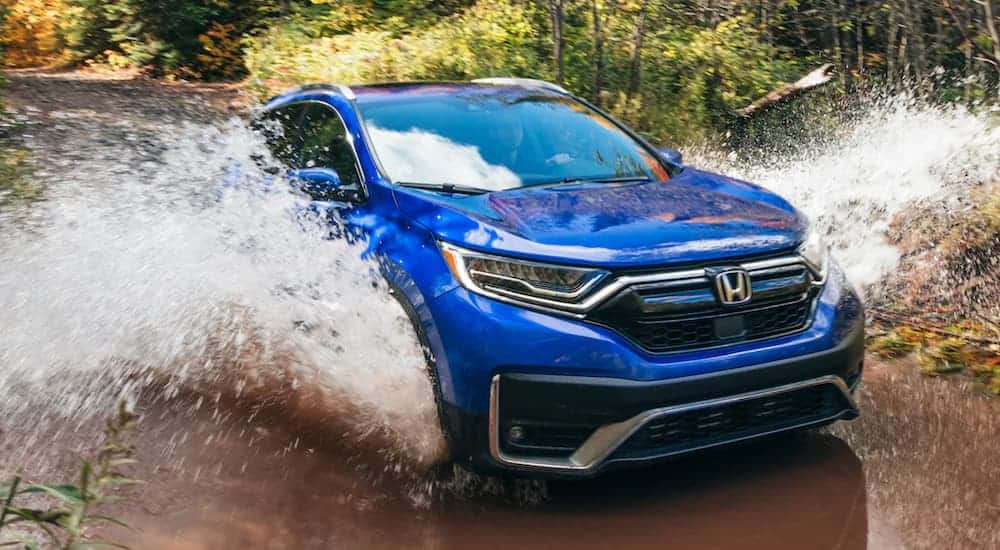 A blue 2021 Honda CR-V Hybrid is shown splashing through a river while off-roading, after leaving an Atlanta CR-V dealer.