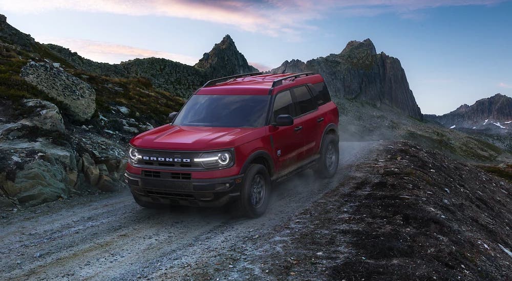 A red 2021 Ford Bronco Sport is driving on a gravel road after leaving a Bronco dealer.