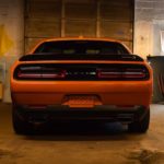 An orange 2021 Dodge Challenger is shown from the rear in a garage.